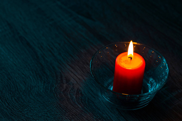 одна красная парафиновая свеча в стеклянных декоративных подсвечниках. яркий красивый свечи свет в темноте. копировальное пространство - Фото, изображение