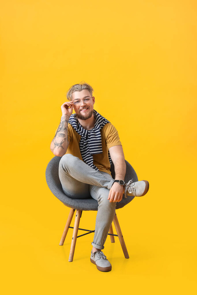 Handsome young man sitting in armchair on color background - Fotografie, Obrázek
