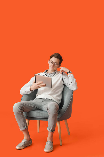 Jongeman met tablet computer zittend in fauteuil op kleur achtergrond - Foto, afbeelding