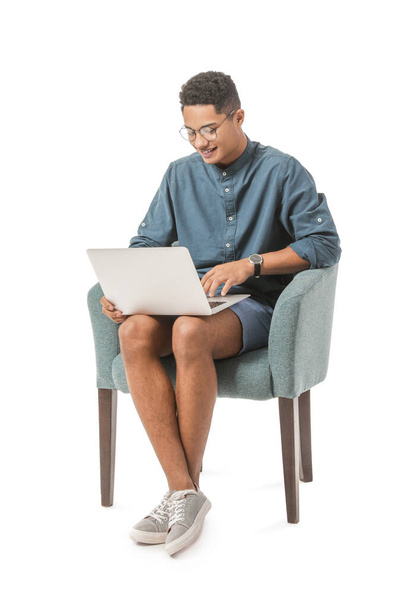 Młody Afroamerykanin z laptopem siedzący w fotelu na białym tle - Zdjęcie, obraz