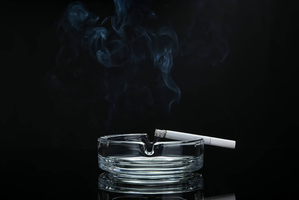 Ash tray with cigarette on dark background - Foto, afbeelding