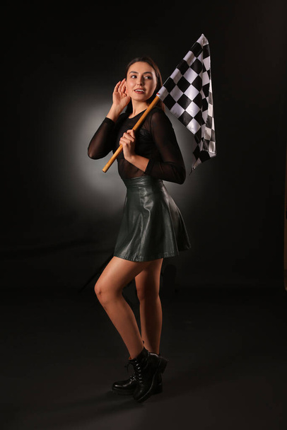 Beautiful young woman with racing flag on dark background - Photo, Image