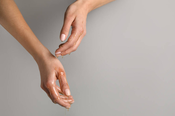 Female hands with dripping honey on grey background - Fotoğraf, Görsel