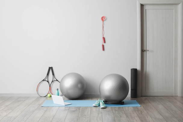 Разнообразное спортивное оборудование с фитнес-шарами и современным ноутбуком возле светлой стены - Фото, изображение
