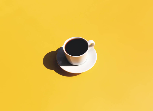 Single white cup and saucer plate of black espresso coffee from top view with shadow of sun on yellow beige terracotta background. High quality photo - Photo, Image