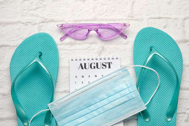 Calendario con accessori da spiaggia e maschera medica su sfondo di mattoni bianchi - Foto, immagini