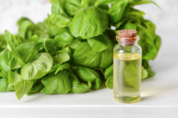 Fresh basil leaves and bottle of essential oil on light wooden background - Photo, Image