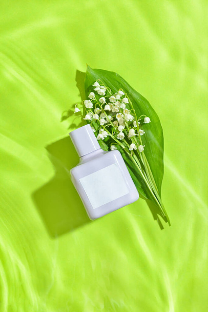 Eine Flasche Parfüm und Maiglöckchen-Blumen in Wasser auf farbigem Hintergrund - Foto, Bild