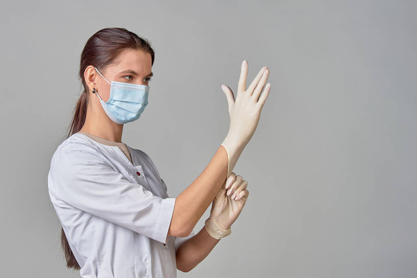 egy orvos fehér köpenyben és orvosi maszkban steril fehér latex kesztyűt tesz a kezére az eljáráshoz, lemásolja a helyet - Fotó, kép