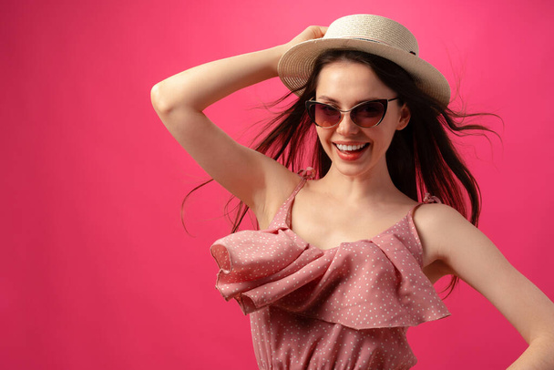 Studio fashion portrait of a young attractive woman in hat and glasses against pink backgorund - Photo, Image