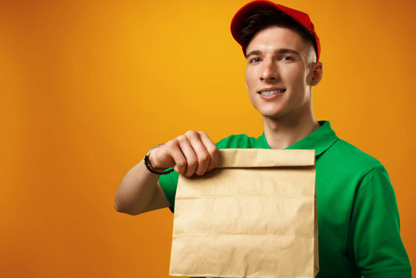 Delivery person holding parcel with food delivery against yellow background - Fotografie, Obrázek
