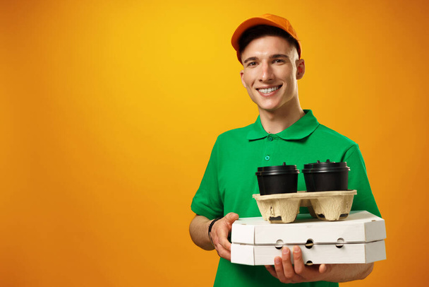 Feliz jovem entregador segurando caixa de pizza contra fundo amarelo - Foto, Imagem