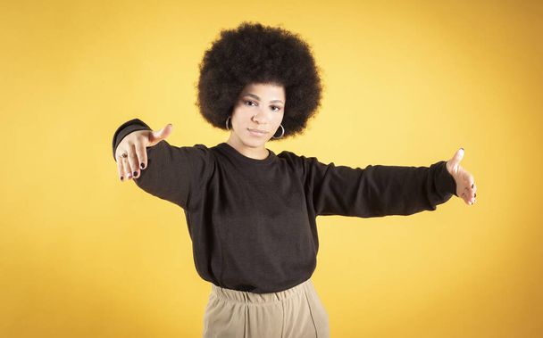 hübsche Afrohaarfrau, macht Umarmungsgeste, gelber Hintergrund - Foto, Bild