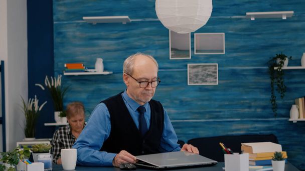 Elderly man freelancer opening laptop squinting while reading emails - Photo, image