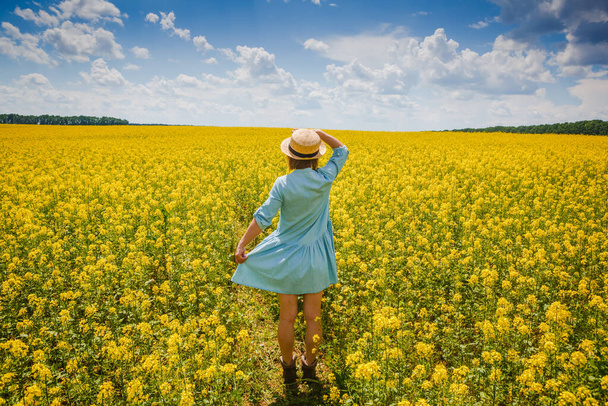 Trendy girl in stylish summer dress with beautiful hat walking in the field with flowers - Foto, Imagen