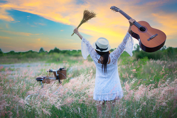 Kobieta szczęśliwa z gitarą na łące. podróże i zachód słońca, miękkie i wybierz focu - Zdjęcie, obraz