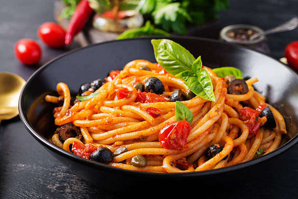 Espaguetis allá puttanesca - plato de pasta italiana con tomates, aceitunas negras, alcaparras, anchoas y albahaca. - Foto, Imagen
