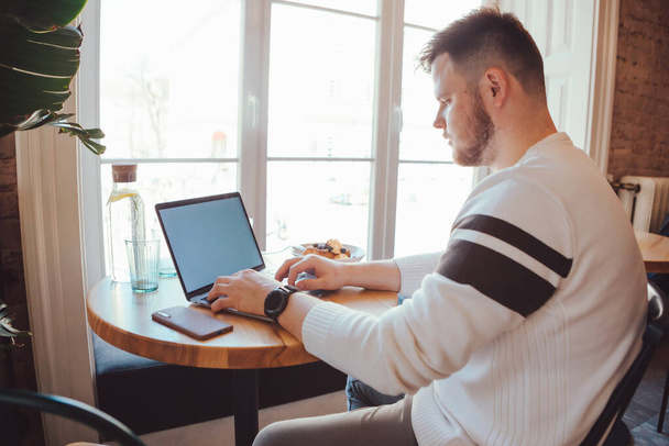 férfi dolgozik laptop kávézóban közel nagy ablak másolás hely távolról működik fehér képernyő - Fotó, kép