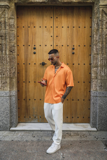 A vertical shot of a male wearing casual clothes and using his phone by an old building in Spain - Фото, изображение