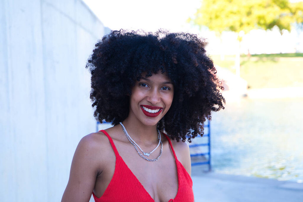 beautiful afro american woman smiling and looking at the camera doing different poses and gestures with her face. The woman is wearing a red top and red lipstick. Concept happiness - Photo, Image
