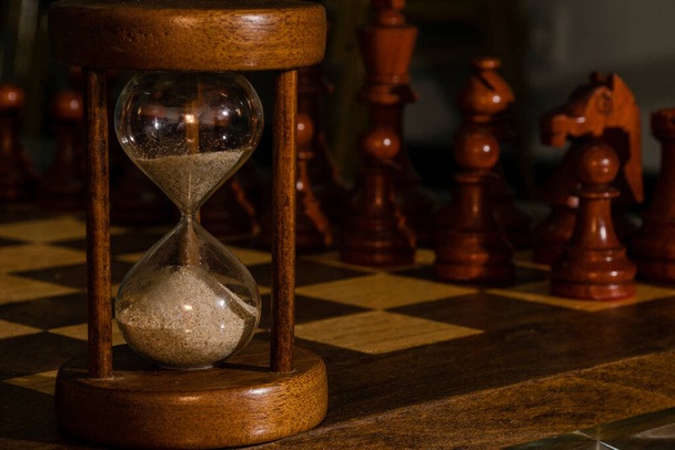 チェスの駒を持つ木製のチェス盤の上の砂時計のクローズアップショット - 写真・画像