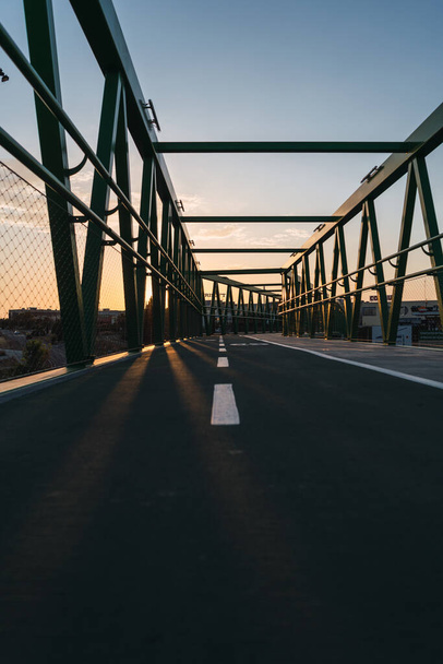 Günbatımı arkaplanlı yeşil metal süspansiyon köprüsünün dikey çekimi - Fotoğraf, Görsel