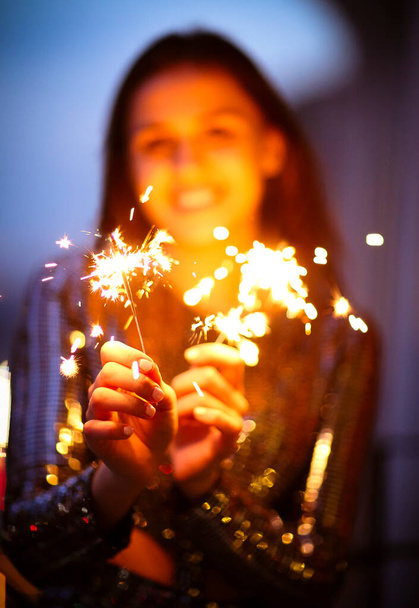 Těší mladá dáma ve večerních šatech s úsměvem a mávání hořící jiskry během sváteční oslavy v noci - Fotografie, Obrázek