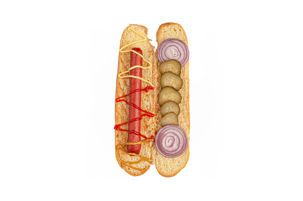 Hot Dog Zutaten. Ein geschnittenes Brötchen enthält die Zutaten: Wurst, Sauce, eingelegte Gurken und Zwiebeln. Blick von oben. Weißer Hintergrund. Isoliert. - Foto, Bild