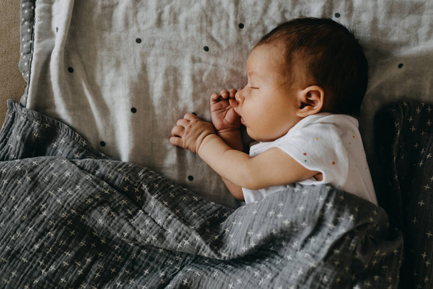 Neugeborenes Baby schläft auf der Seite, bedeckt mit einer grauen Decke. - Foto, Bild