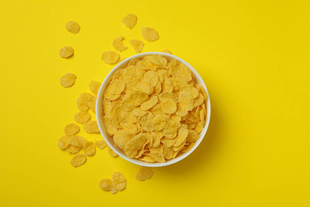 Bowl of corn flakes on yellow background - Фото, изображение