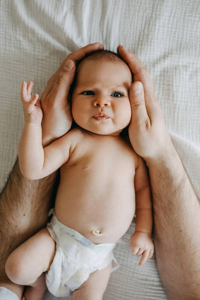 Nowo narodzone dziecko w pieluszce, śmieszna twarz, patrząc w kamerę, trzymane przez ojca. - Zdjęcie, obraz