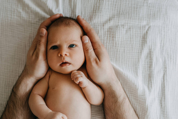 Portrait de bébé nouveau-né, regardant la caméra, tenu par son père. - Photo, image