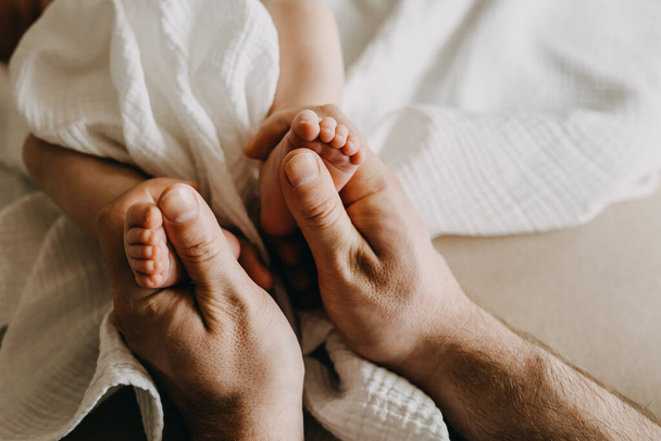 lähikuva isästä, jolla on pienet vastasyntyneet vauvan jalat suurissa käsissä. - Valokuva, kuva
