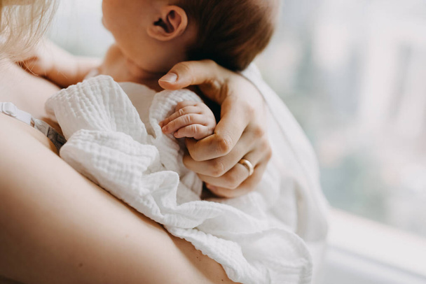 Primer plano de la madre sosteniendo la mano del bebé recién nacido, de pie junto a la ventana. - Foto, imagen