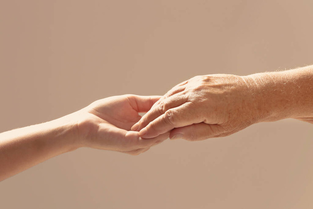 Helping hands on beige background, closeup. Elderly care concept - 写真・画像