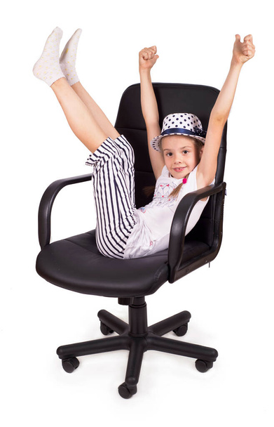 Офисное кресло офисного кресла и маленькая веселая девочка подняли ноги изолированно на белом фоне. Современное регулируемое кресло из черной кожи. - Фото, изображение