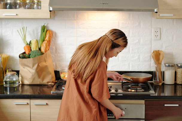 Młoda kobieta włącza kuchenkę gazową, aby smażyć warzywa lub zrobić sos makaronowy na obiad, widok z tyłu - Zdjęcie, obraz