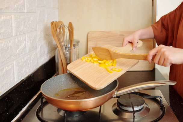 Yemek pişirirken sarı dolmalık biberi sebze yağıyla kızartan genç bir kadının yakın plan resmi. - Fotoğraf, Görsel
