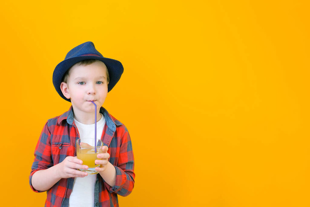 A boy in a hat drinks juice with a straw. Relaxing concept. Yellow background Place for your text - Φωτογραφία, εικόνα