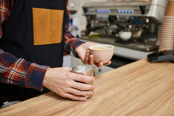 male waiter in apron holding cup of hot drink - Foto, afbeelding