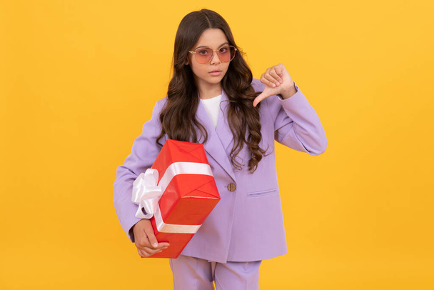 trendige Kind in Sonnenbrille und Anzug Zeigefinger Geschenk-Box auf gelbem Hintergrund, Verkauf - Foto, Bild