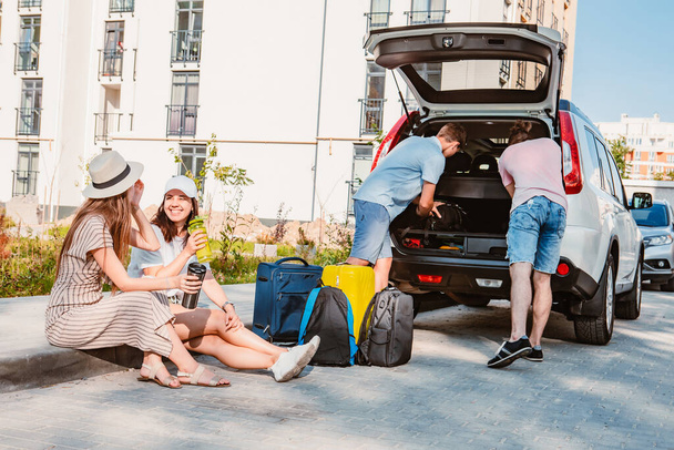 φίλοι φορτώνουν πορτ-μπαγκάζ αυτοκινήτου με αποσκευές. καλοκαιρινές διακοπές με αυτοκίνητο. - Φωτογραφία, εικόνα