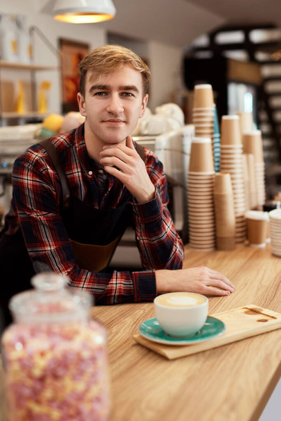 happy male waiter in apron holding cup of hot drink - Foto, Imagen