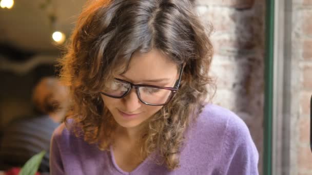 Mujer joven toma notas en almohadilla sentado en el alféizar de la ventana del café - Metraje, vídeo