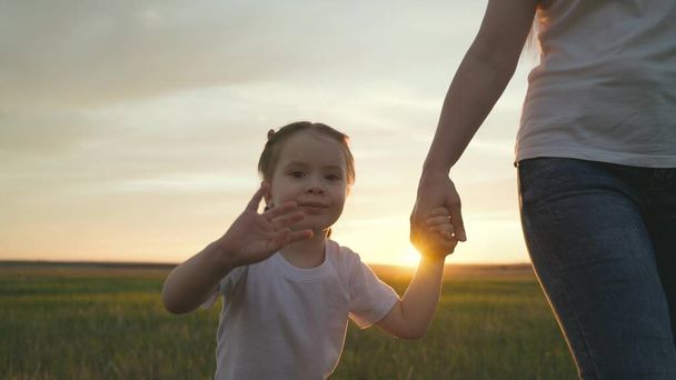 Mamá lleva a una niña por la mano, agitando su mano en el resplandor de la puesta del sol, un sueño de ser una familia feliz, un primer plano de un niño sonriente, tomar una mano de los niños en una mano mayor, el amor maternal y - Foto, imagen