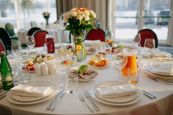 A servir a mesa de casamento. Negócios de restaurantes. Copos, pratos brancos e talheres em uma mesa redonda decorada com rosas em uma toalha de mesa branca. - Foto, Imagem