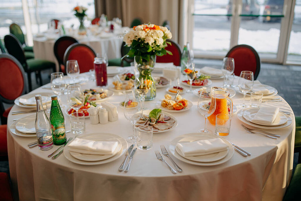 Sirviendo la mesa de bodas. Negocios de restaurantes. Vasos, platos blancos y cubiertos sobre una mesa redonda decorada con rosas en un mantel blanco. - Foto, imagen