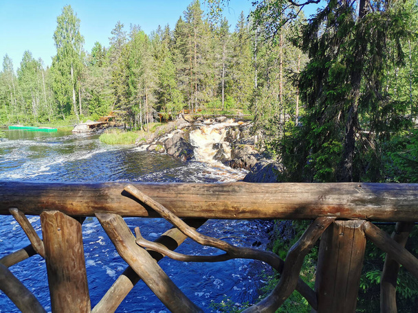 Widok z tarasu widokowego malowniczego wodospadu na rzece Tokhmayoki w Karelii, otoczony drzewami w pogodny letni poranek. - Zdjęcie, obraz