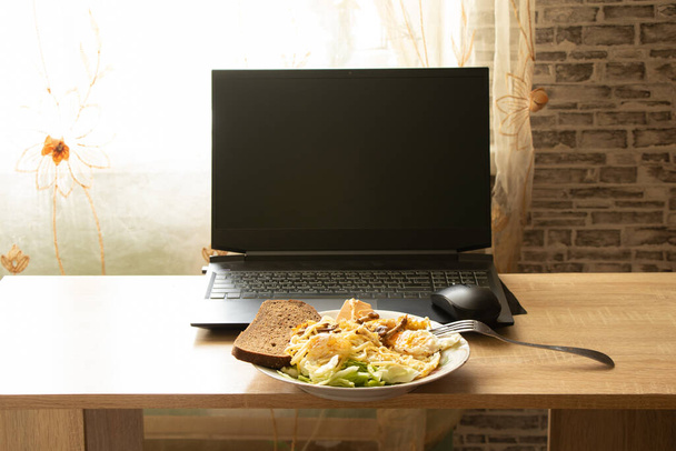 talerz z makaronem jajecznym i sałatką z kawałkiem czarnego chleba na pulpicie w domu przynieśli laptopa, obiad podczas pracy przy komputerze, praca online - Zdjęcie, obraz