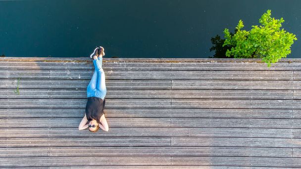 Vacation, enjoyment and freedom concept. Top aerial view from drone lifestyle portrait of young woman on a wooden riverside next to the water of the river. - Photo, Image